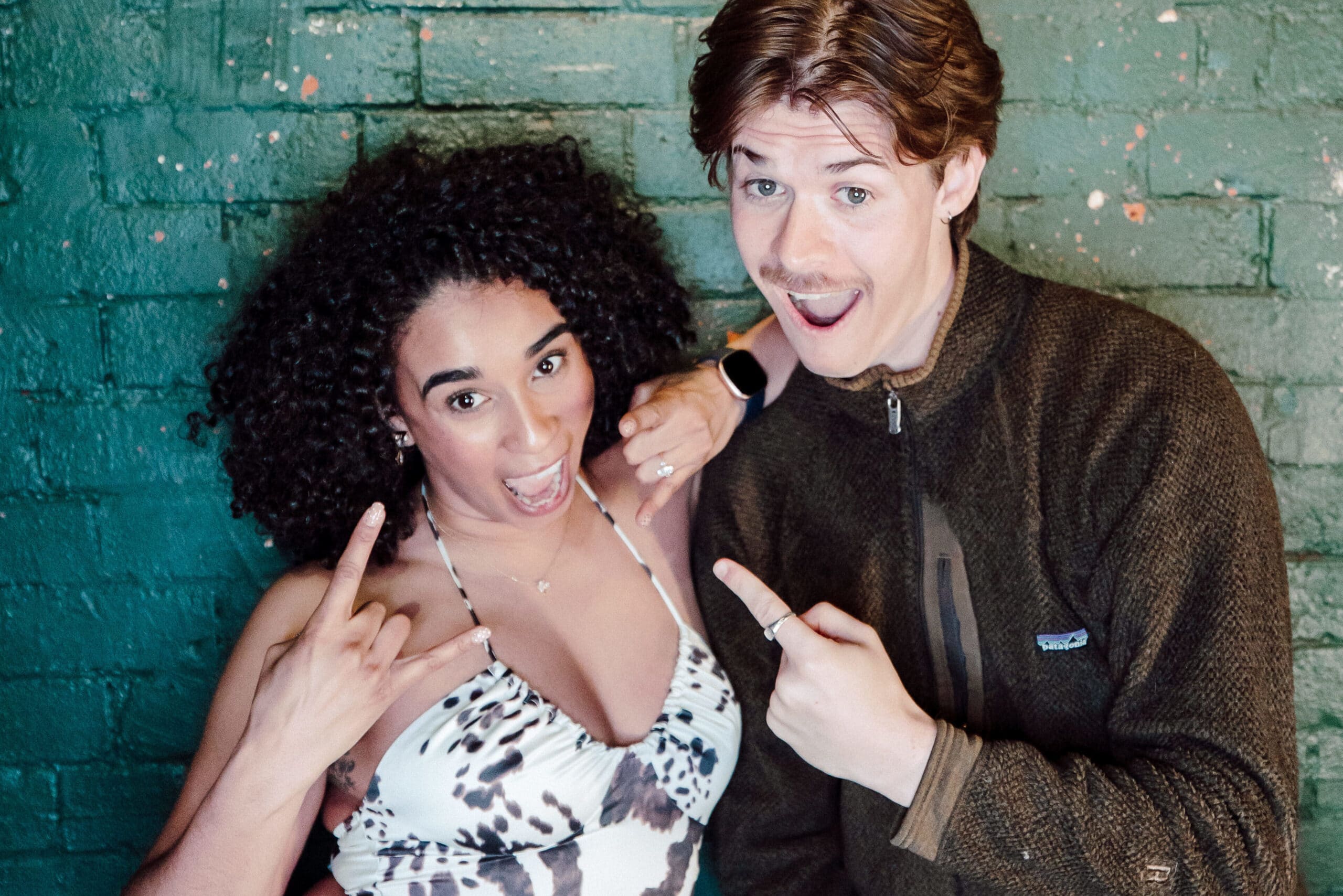 Man and woman posing for a photo in front of a blue-green brick wall