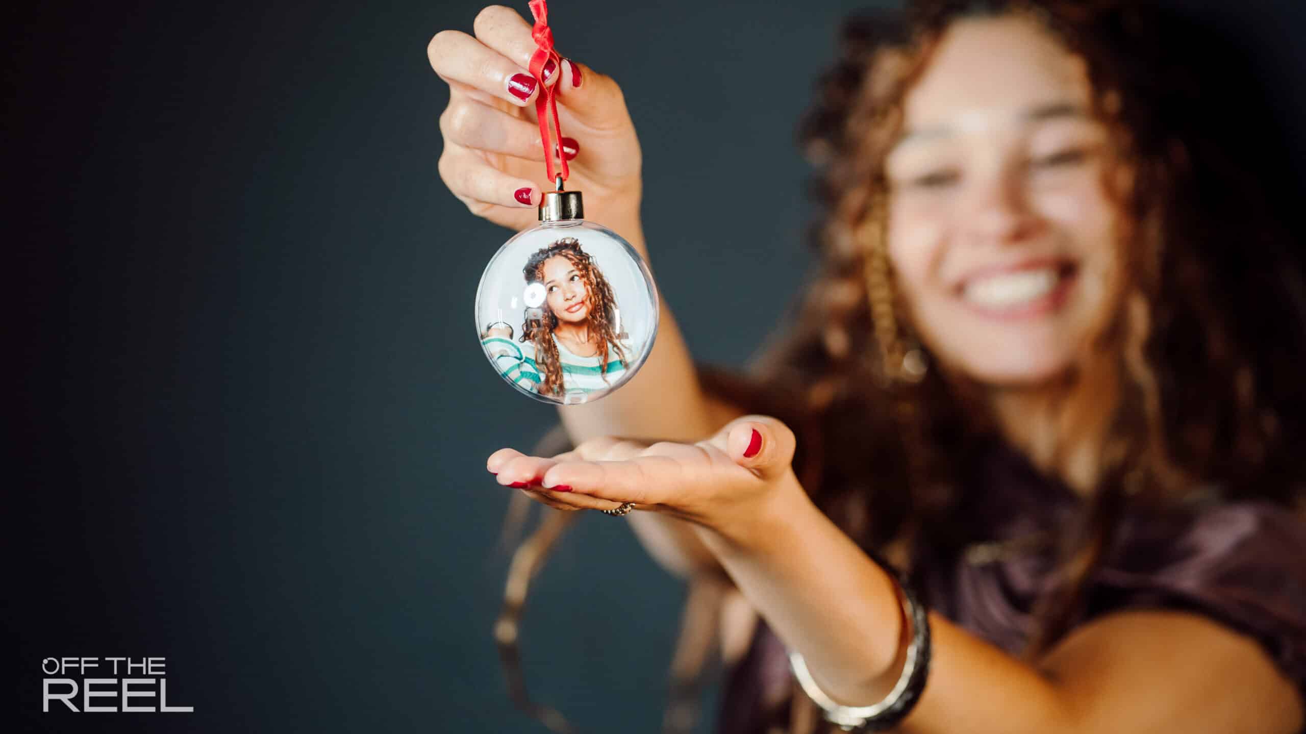 A delighted woman holds up her personalised holiday bauble featuring her own photo inside